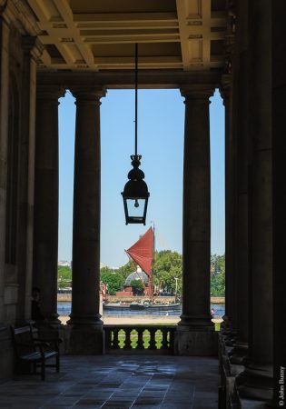 The Painted Hall in the Old Royal Naval College, Greenwich, was completed by Christopher Wren and Nicholas Hawksmoor in 1703. This view towards the Thames is through the colonnade at the entrance to the hall. A Thames sailing barge is passing. (May10)