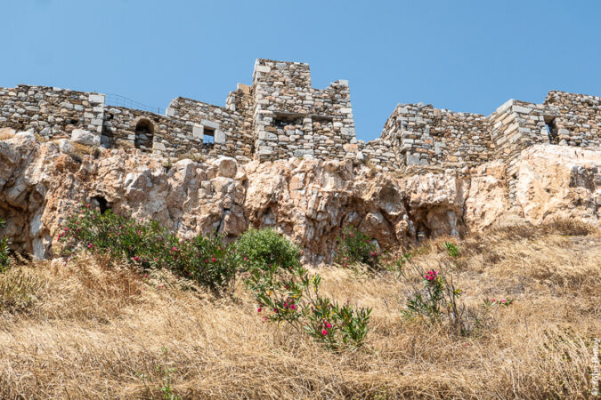 Looking up at the partially restored castle walls built on rock at the top of the hill above the Chora. (Jun23)